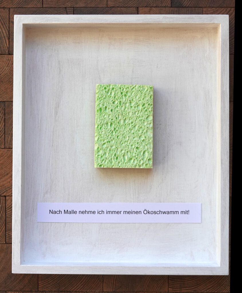 Malle. 2024, Berlin. Eco-sponge, text on paper, painting body, 24 x 30 x 3 cm. An eco-sponge made of cellulose and coconut fibers sticks in the middle of the open box above the text 